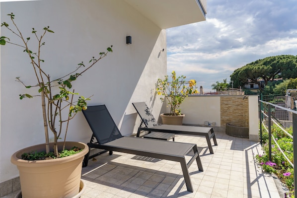 Un balcón con dos sillones de descanso, una planta en maceta y vistas del entorno.