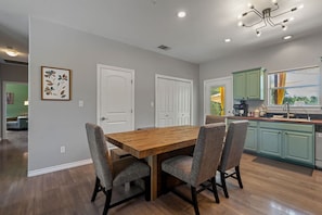 A dining area with a wooden table and four chairs, a kitchen with green cabinets, and a window with a view.