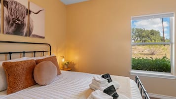 Une chambre à coucher avec un lit, des oreillers, une table de chevet, une lampe et une fenêtre donnant sur l’extérieur.