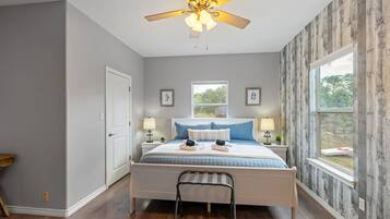 Un dormitorio con cama, mesitas de noche, ventilador de techo y ventana.