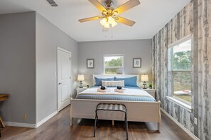 Un dormitorio con cama, mesitas de noche, ventilador de techo y ventana.