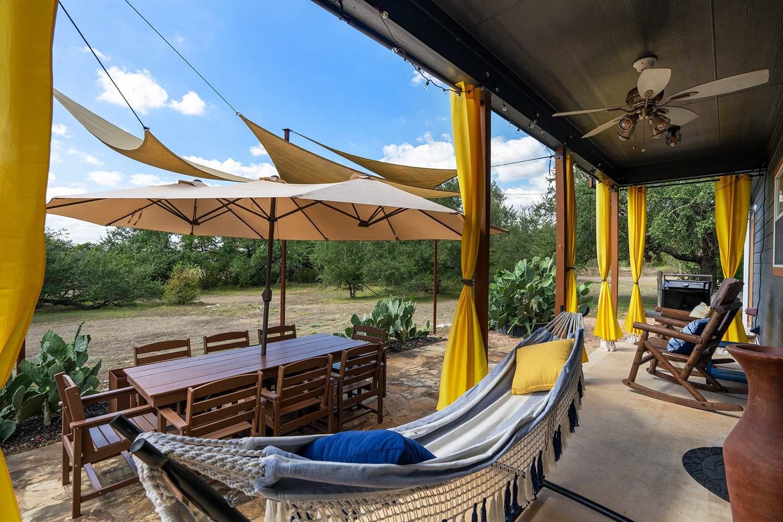 An outdoor patio with a table, chairs, a hammock, and yellow curtains.