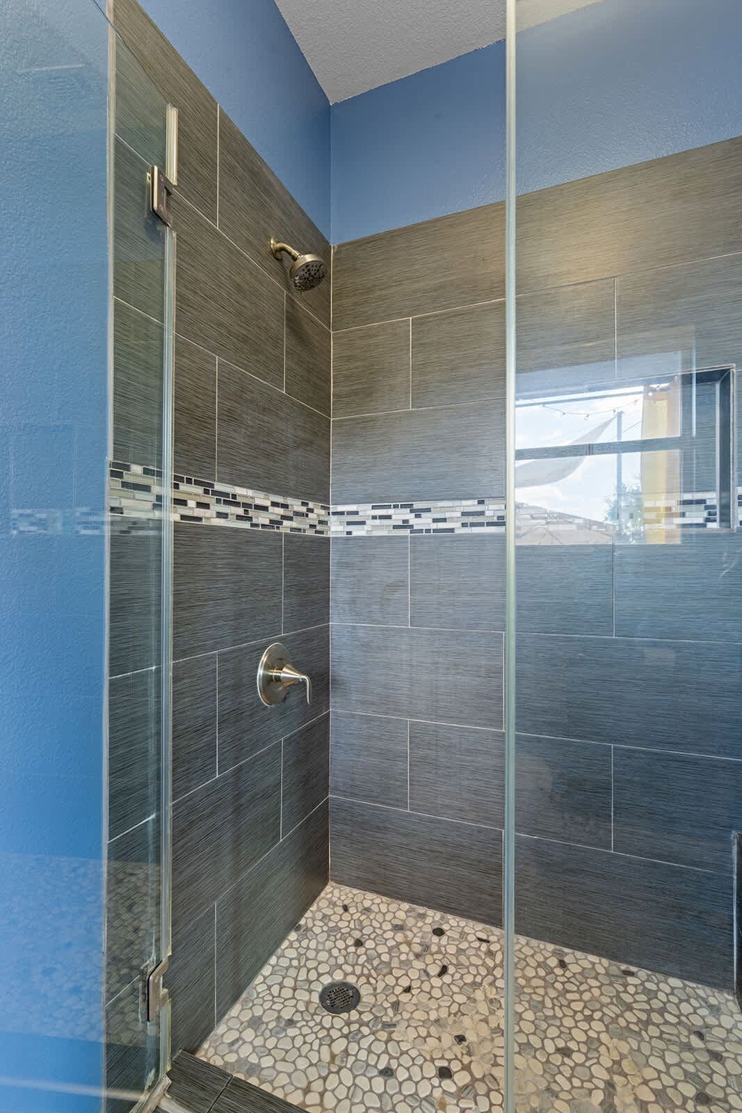 A shower with a glass door, tiled walls, and a pebble-patterned floor.