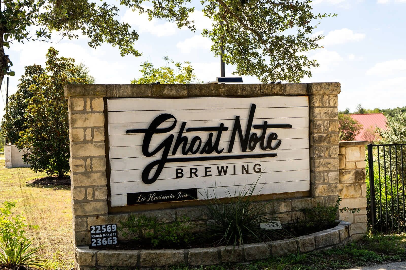 A sign for Ghost Note Brewing with a rustic stone wall and a clear sky in the background.