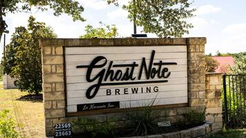 A sign for Ghost Note Brewing with a rustic stone wall and a clear sky in the background.