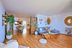 A modern living room with a blue sofa, wooden coffee table, and a dining area with a wooden table and chairs. - Le Balcon des Sanguinaires - Vue sur la mer (Ajaccio)
