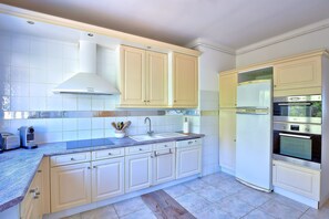 A kitchen with white cabinets, a double sink, a refrigerator, and an oven. - Le Balcon des Sanguinaires - Vue sur la mer (Ajaccio)