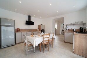 A modern kitchen with a dining area, featuring a refrigerator, stove, and coffee machine. - Le Clos d'Adèle - Maison climatisée pour 8 (La Neuville-Bosmont)