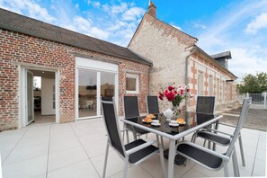 Une terrasse avec une table et des chaises, un bâtiment en briques et un ciel dégagé.