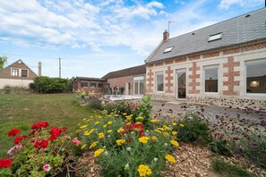 A residential property with a brick facade, a visible chimney, and a garden with various flowers. - Le Clos d'Adèle - Maison climatisée pour 8 (La Neuville-Bosmont)