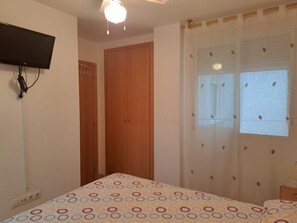 Een slaapkamer met een bed, een aan de muur bevestigde televisie, een raam met gordijnen en een deur.