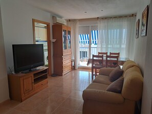 A living room with a television, wooden furniture, a sofa, and a balcony with striped curtains. - Mediterranean Vacation Rental (Valencia) – Just 100 m from the Beach (Platja de Nules)