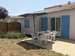 A patio with a table and chairs, a wooden fence, and a building with blue shutters. - Le Green de Pornic - A 2km du Port (Pornic)