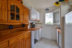 A compact kitchen with wooden cabinets, a coffee maker, and a window with a view of a building. - Le Green de Pornic - A 2km du Port (Pornic)