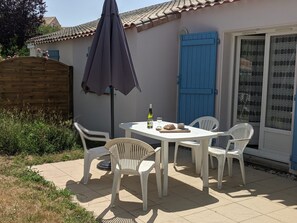 An outdoor patio with a white table and chairs, a bottle of wine, and a loaf of bread. - Le Green de Pornic - A 2km du Port (Pornic)