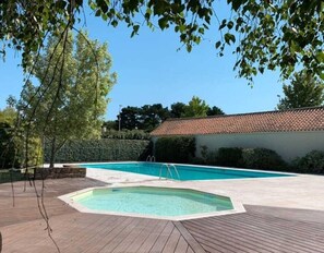 A swimming pool with a wooden deck, surrounded by greenery and a building with a tiled roof. - Le Green de Pornic - A 2km du Port (Pornic)