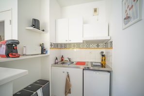 Une cuisine compacte avec des meubles blancs, une machine à café Bosch, un évier et un égouttoir à vaisselle.
