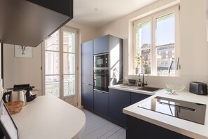 A modern kitchen with a built-in oven, a sink, and a window overlooking a cityscape. - Le 50 Emeraude - 200m de la Plage (Dinard)