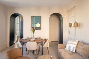 A dining area with a round table, chairs, and a vase of flowers. There is a painting on the wall and a door in the background. - Le 50 Emeraude - 200m de la Plage (Dinard)