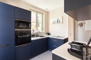 Eine moderne Küche mit dunklen Schränken, einem Bosch-Ofen, einer Nespresso-Maschine und einem Fenster mit grünen Rollläden.