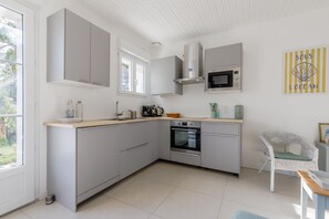 A modern kitchen with grey cabinetry, a built-in oven, a microwave, and a window providing natural light. - Le Répit familial - Maison avec Jardin pour 6 (Saint-Jean-de-Monts)