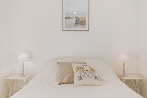 Ein Schlafzimmer mit einem Bett, zwei Nachttischen, einer Lampe auf jedem Tisch und einem gerahmten Bild an der Wand.