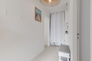 A narrow hallway with a white door, a shower curtain, a framed picture on the wall, and a small white cabinet with a plant. - Le Répit familial - Maison avec Jardin pour 6 (Saint-Jean-de-Monts)