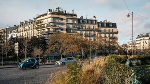 Un edifici d'apartaments de diversos pisos amb balcons, un carrer empedrat i cotxes aparcats.