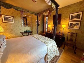 Ein traditionelles Himmelbett mit Baldachin, ein Spiegel darüber und ein Nachttisch mit Lampe.