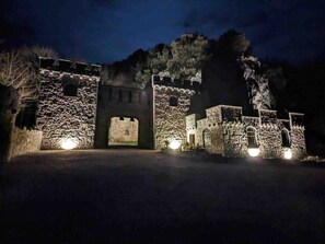 Eine steinerne Burg mit einem großen Tor und mehreren kleineren Gebäuden, beleuchtet durch künstliches Licht.