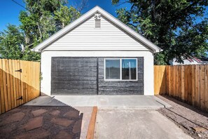 Eine Garage mit dunkler Fassade und einer klaren Fensterscheibe, umgeben von einem Holzzaun und einem gepflasterten Auffahrt.
