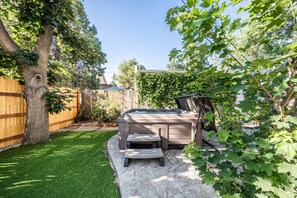 Ein Garten mit Whirlpool, einer Holzterrasse und einem gepflegten Rasen.