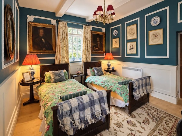 Ein Zimmer mit zwei Betten, einer Chandelüster und gerahmten Kunstwerken an den Wänden.
