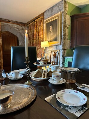 Ein elegantes Esszimmer mit Steinwand, einem Porträt und einem Tisch, der für ein Kaffeetrinken mit Sandwiches und Scones gedeckt ist.