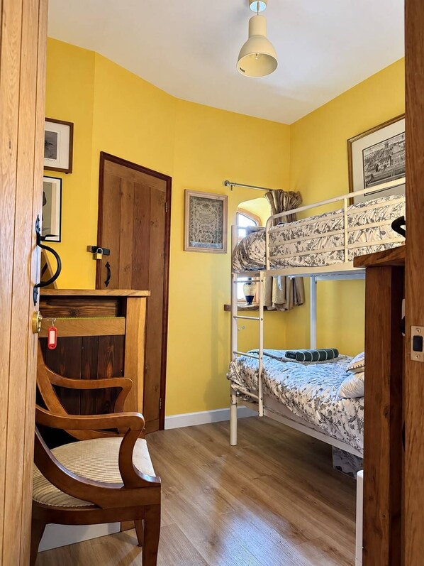 Ein Zimmer mit einem Etagenbett, einem Holztisch mit Stuhl und einer Tür mit Schloss.