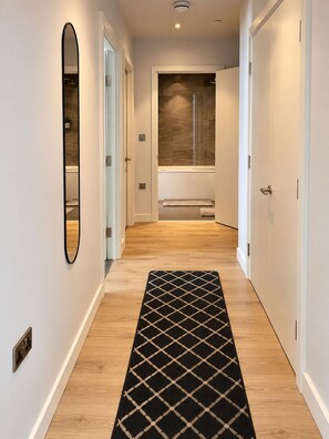 A hallway with a black and white patterned rug, white walls, and a wooden floor. - Luxury 2-Bed Apartment in Manchester City Centre (Manchester)