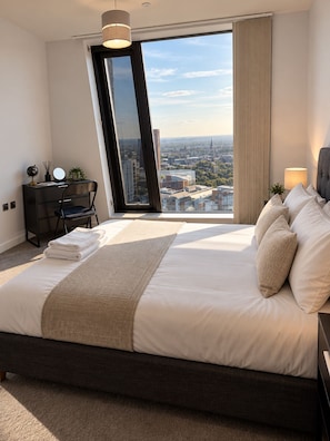 A modern hotel room with a large bed, a desk, and a view of the cityscape. - Luxury 2-Bed Apartment in Manchester City Centre (Manchester)
