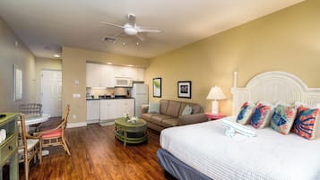 A bedroom with a bed, a dining table with chairs, a kitchen area, and a ceiling fan.