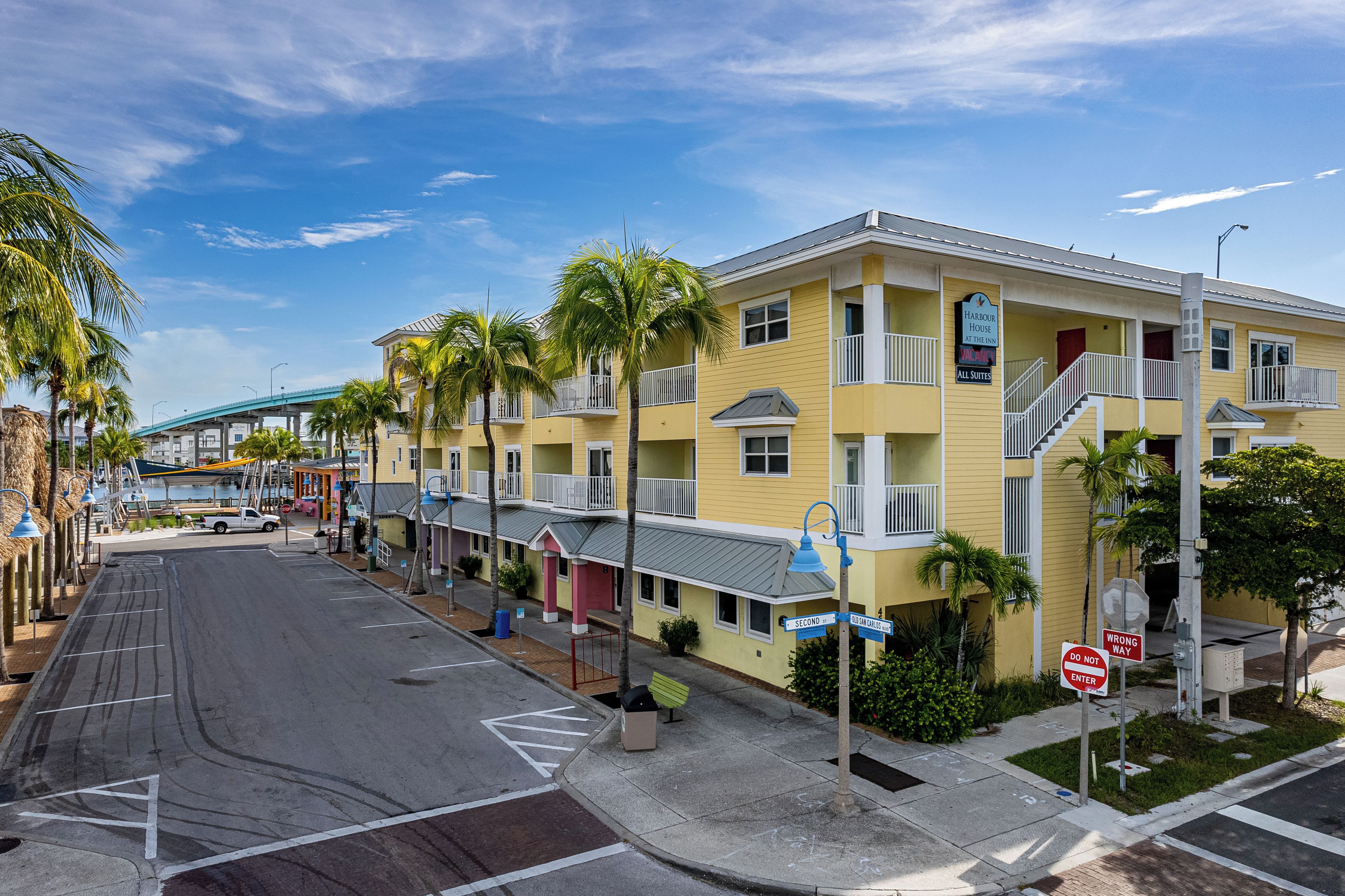 A yellow multi-story hotel with balconies, a covered walkway, and a sign indicating availability.