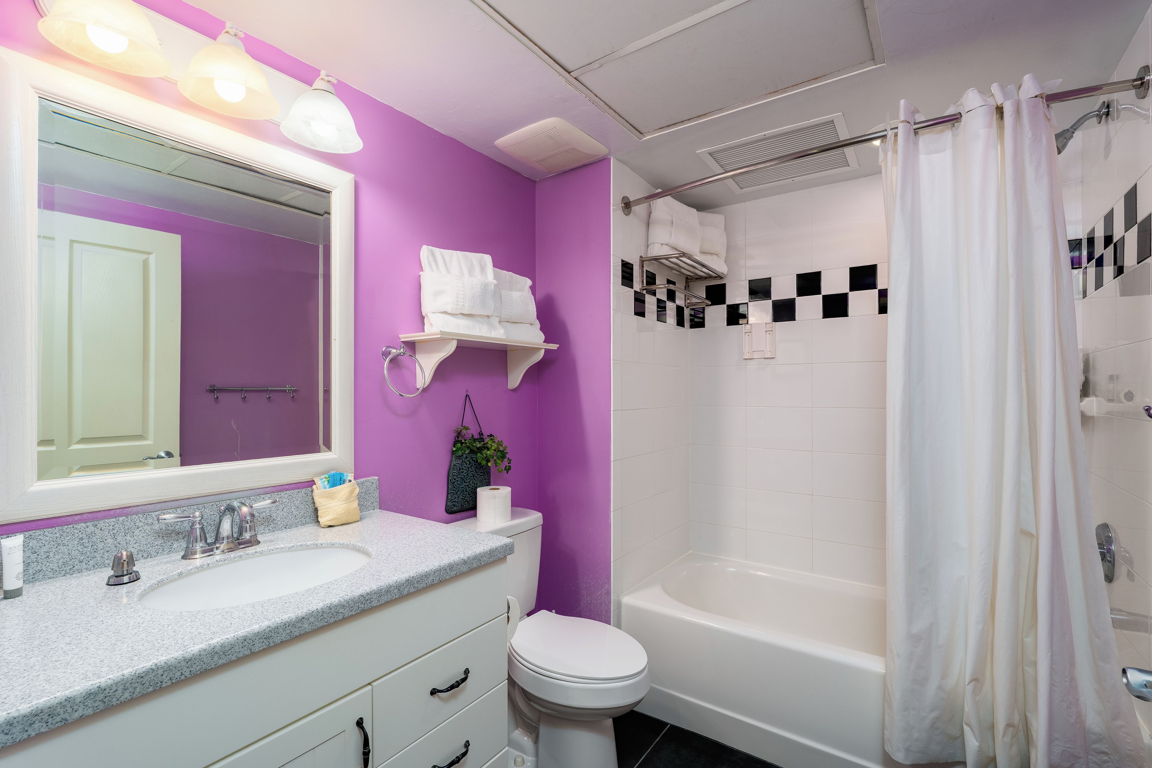 A bathroom with a purple wall, white fixtures, a sink with a mirror, a toilet, and a bathtub with a shower curtain.