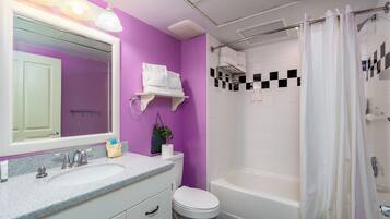 A bathroom with a purple wall, white fixtures, a sink with a mirror, a toilet, and a bathtub with a shower curtain.