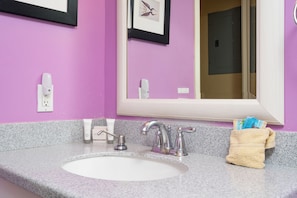Een badkamer met een wit wastafelmeubel, twee kranen, een lijst met foto aan de muur en een handdoekhouder met toiletartikelen.