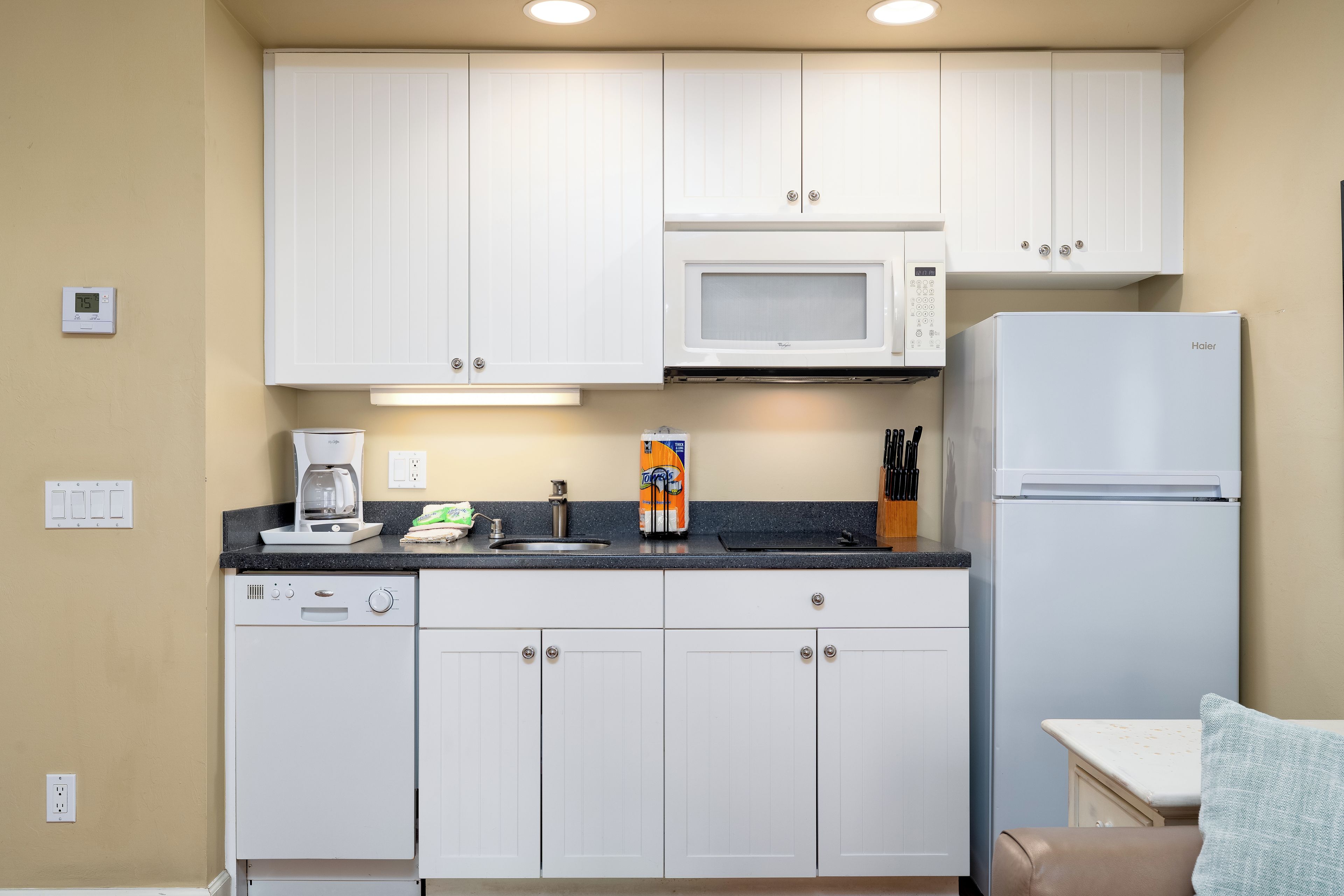 A compact kitchen with white cabinets, a microwave, a refrigerator, and a coffee maker on the counter.