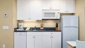 A compact kitchen with white cabinets, a microwave, a refrigerator, and a coffee maker on the counter.