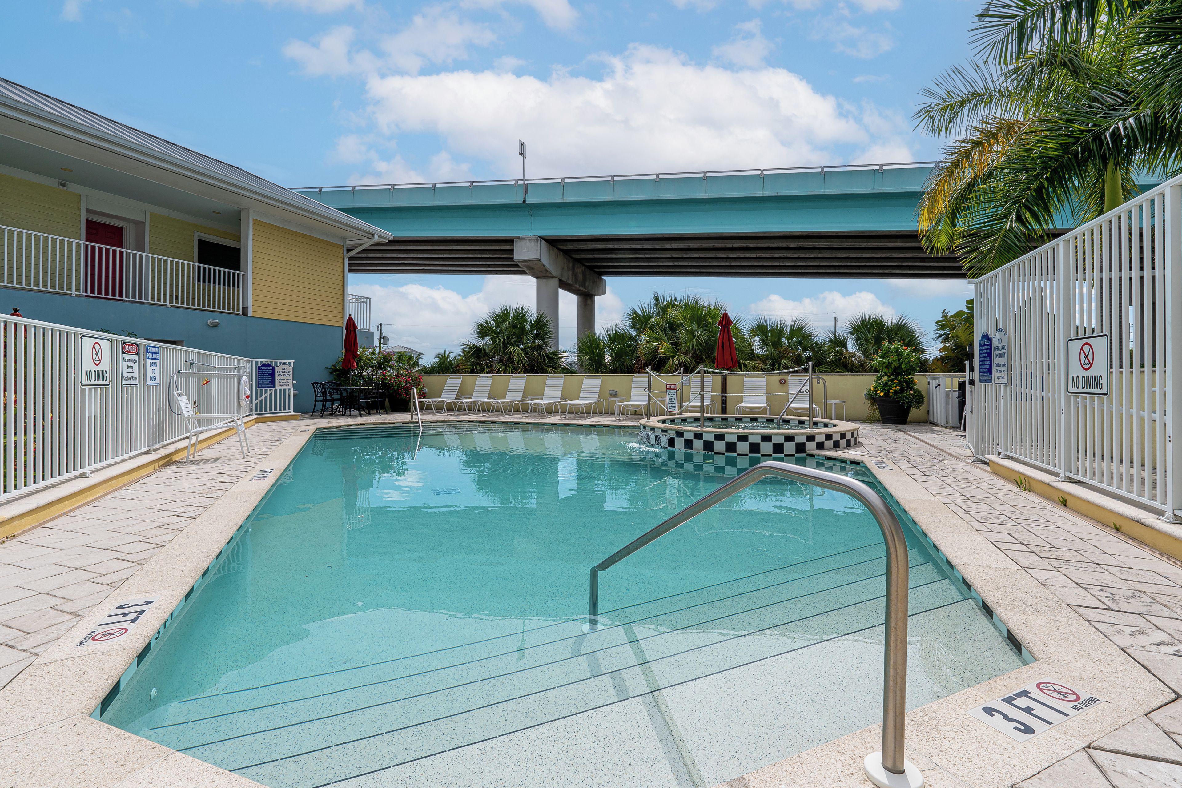 Une piscine avec un plongeoir, des chaises longues et un espace abrité avec des parasols.