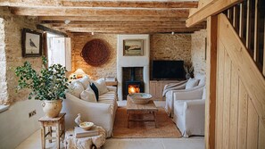 A rustic living room with a stone wall, a fireplace, a television, and a cozy seating area. - The Little Cottage Kingham (Kingham)
