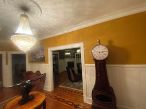 Ein Zimmer mit einer Chandelüster, einer Standuhr und einer Tür zu einem weiteren Raum.