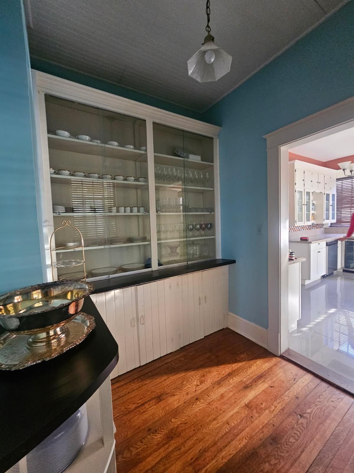 Een keuken met houten kastjes, een zwart aanrecht en een glazen vitrine met servies.