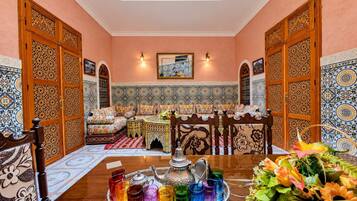 A traditional Moroccan room with a sofa, a dining table with a tray of colorful glasses, and a decorative wall.