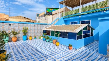 A courtyard with a blue tiled floor, potted plants, and a building with a blue facade and a balcony.